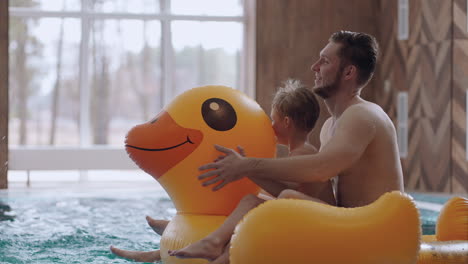 happy dad and little son are riding funny inflatable duck in swimming pool have fun and rest in weekend