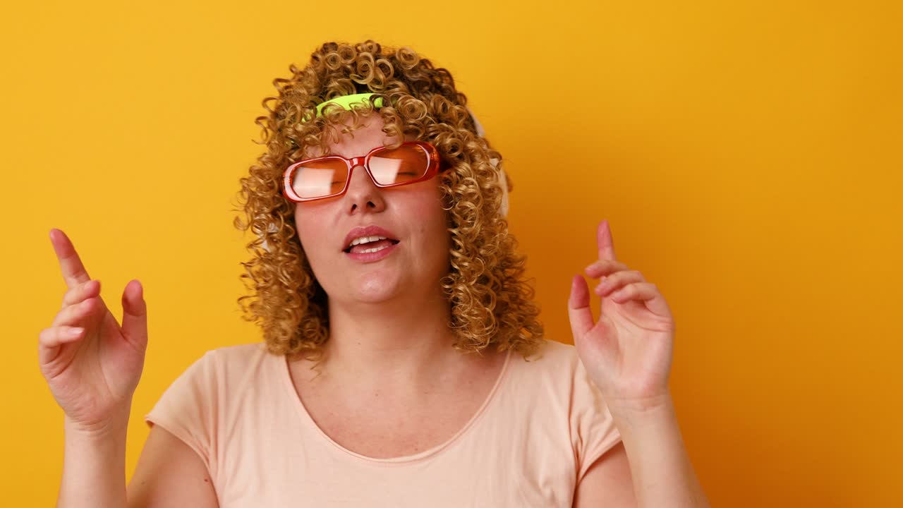 divertida alegre chica de cabello ondulado con gafas y un vendaje escuchando el alma bailando divirtiéndose aislada sobre fondo de color amarillo
