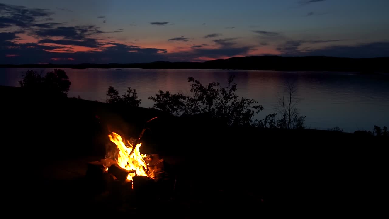 Philip Edward, Island, Ontario, Canada - The fire catching the gas being thrown in the air by a person in a lakeside - wide shot