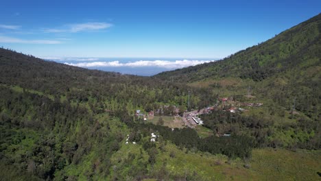 aerial footage over the forest and a village with the clouds in the background.