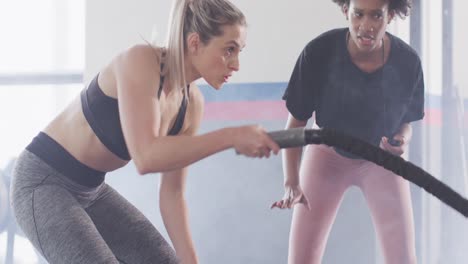 video de una entrenadora de fitness femenina diversa con un cronómetro y una mujer luchando con cuerdas trabajando en un gimnasio.