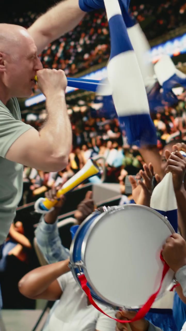 Verticaal filmpje: Energieke mannelijke voetbalfan blaast op een blauwe vuvuzela op een stadiontribune.