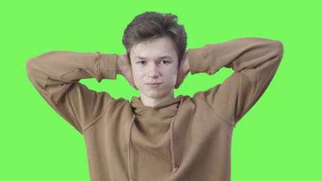 boy closing ears with hands and gesturing no by shaking head. portrait of caucasian teenage college student disagreeing at greenscreen background. adolescence, disagreement, objection. chromakey.