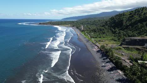 anjouan island's black sand beach with ocean waves and lush greenery, aerial view