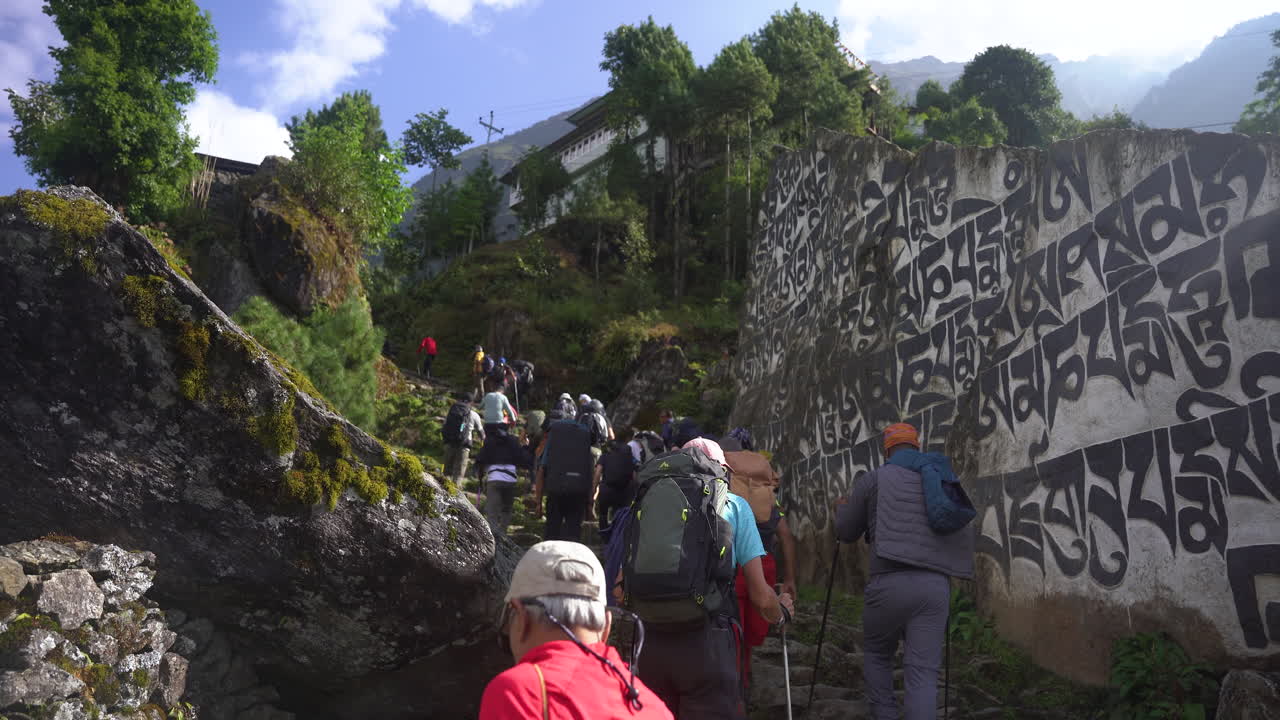 Tourists forming a group on the Everest Base Camp trek, walking along ladder trails with stone walls engraved with Himalayan literature, embracing spiritual beliefs and adventure