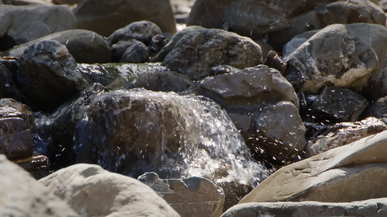 Slow motion shot of a small waterfall over some stones in a river bed. Water also splashes upwards from the waterfall.