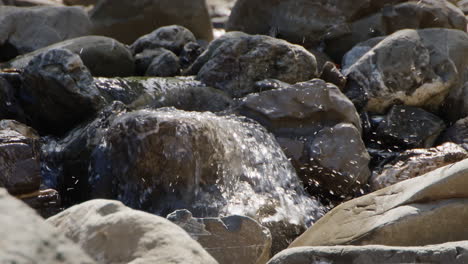slow motion shot of a small waterfall over some stones in a river bed. water also splashes upwards from the waterfall.