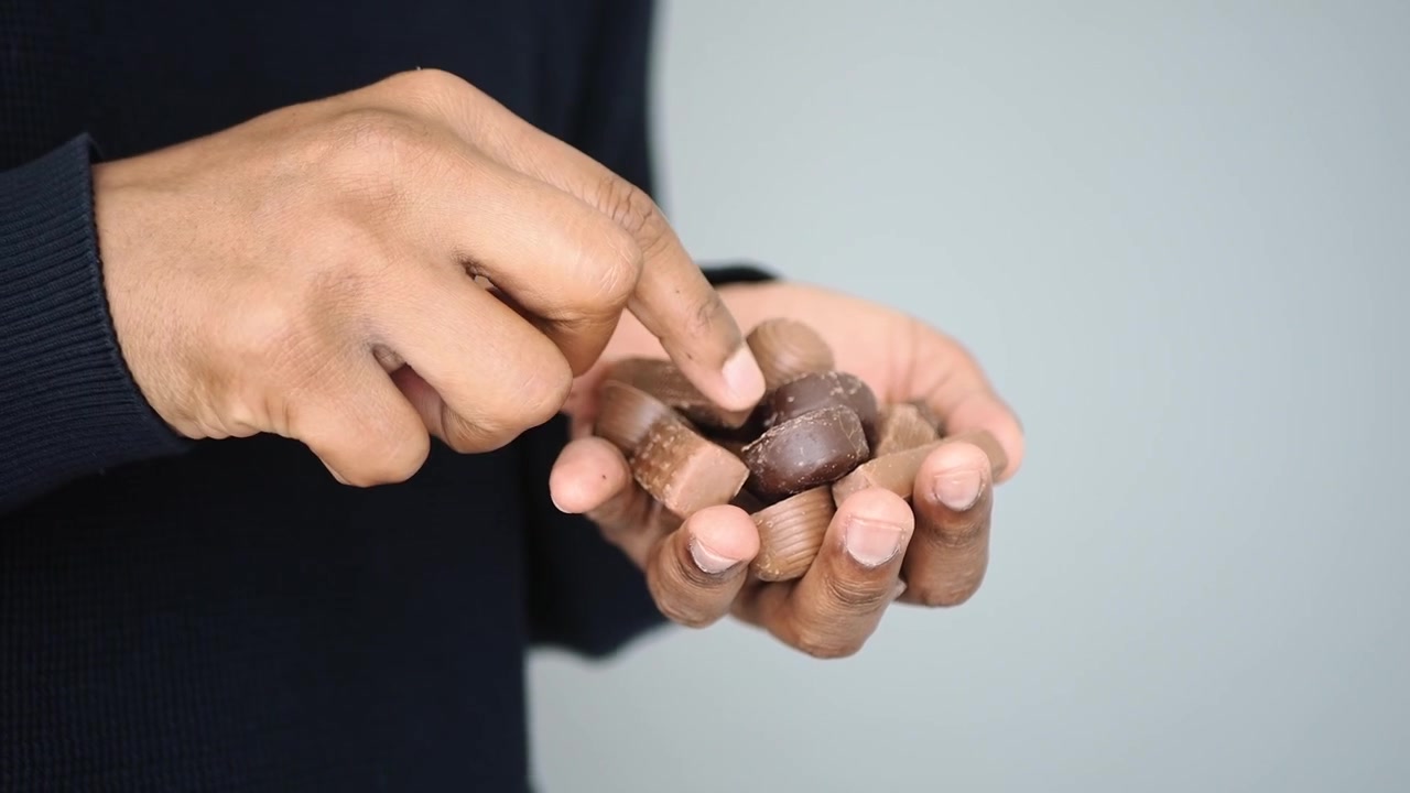 Cận cảnh bàn tay đang cầm và nhặt một viên sô cô la