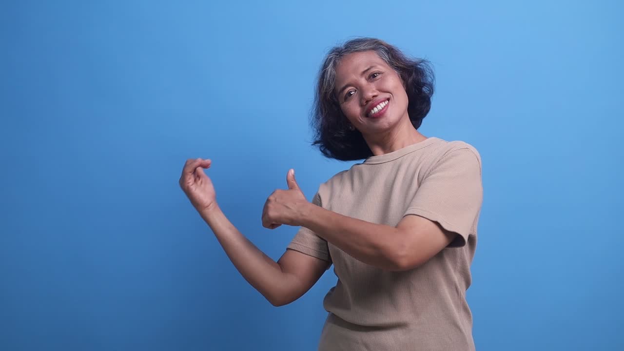 Middle age Asian woman smiling presenting to the side on copyspace over isolated blue background