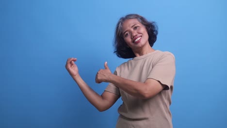 middle age asian woman smiling presenting to the side on copyspace over isolated blue background