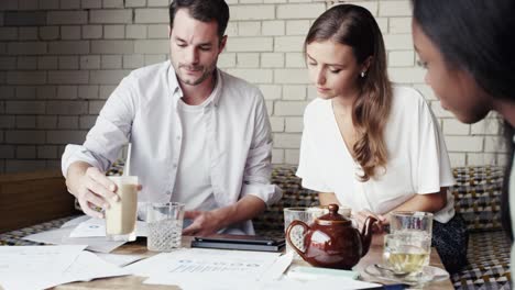 imágenes de video en 4k de un grupo diverso de empresarios sentados juntos en un café y usando una tableta digital durante una discusión