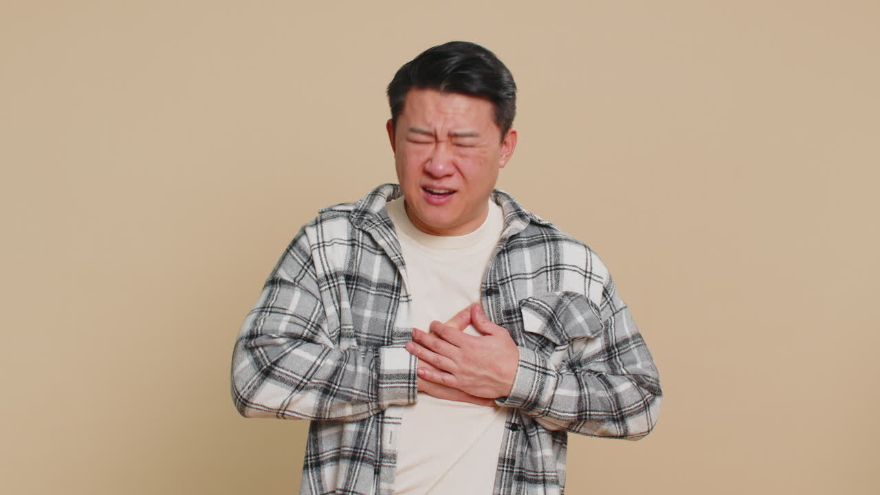 Stressed ill sick asian man suffers from tension holding chest with heart pain attack risk of stroke
