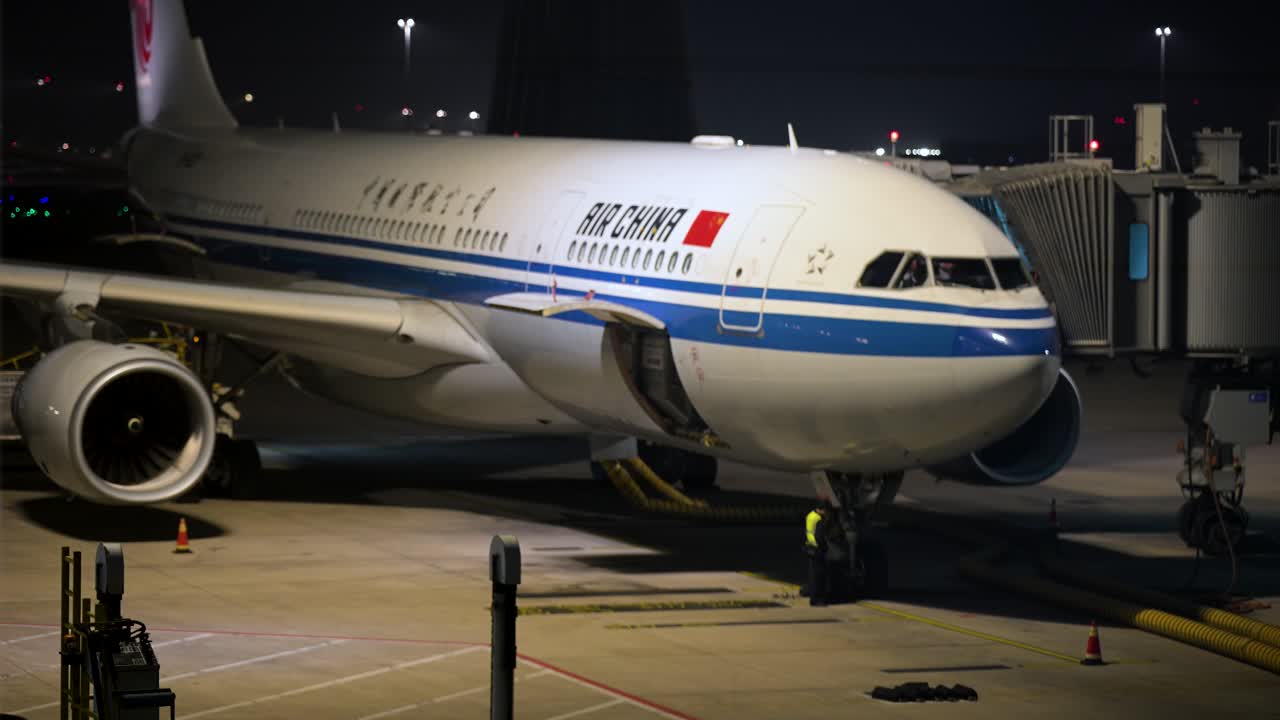 At night, an Air China jet is stationed on a runway at Beijing International Airport, illuminated by runway lights.