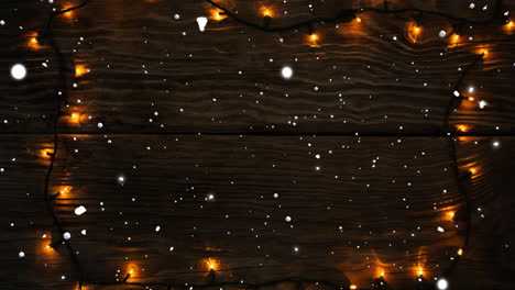 animation of snow falling over fairy lights on wooden background with copy space at christmas