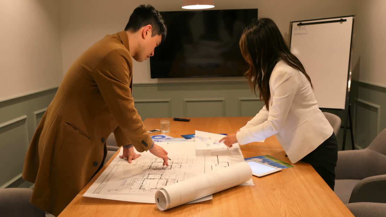 Side view of young Asian business people discussing over blueprint in the conference room 4k