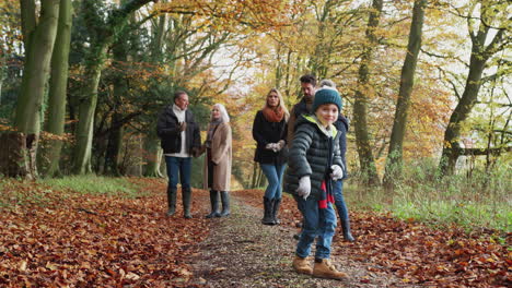 multi-generation family walks along path through autumn countryside as grandson dances in foreground