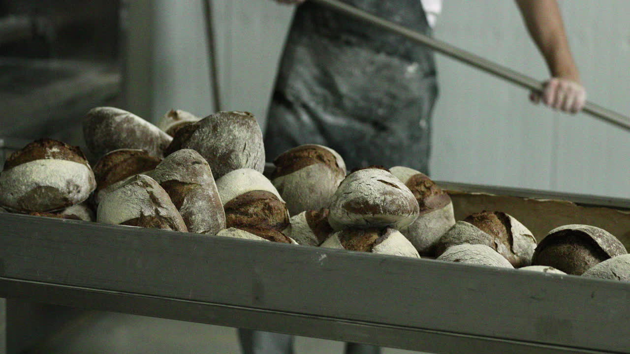 пекарь вынимает из духовки свежевыпеченный хлеб и переносит его на стол