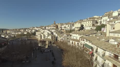 Drone-shot-of-white-houses-in-Cazorla-city-in-Jaen,-Andalusia,-Spain-situated-on-a-steep-hill,-olive-groves-in-the-distance