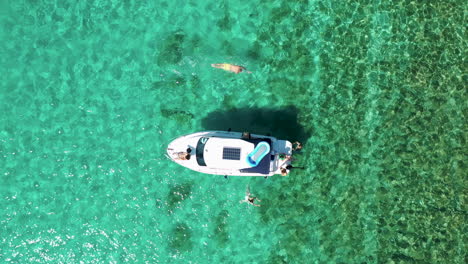 people swim next to boat anchor in blue sea during summer in blue lagoon, croatia. - aerial, top down