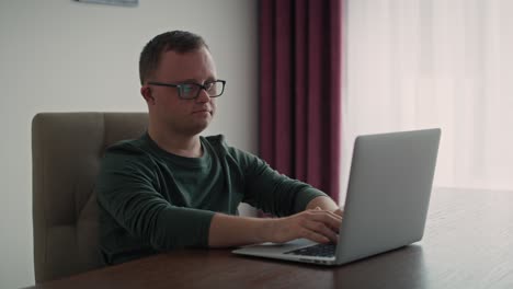 hombre caucásico adulto con síndrome de down usando una computadora portátil en casa.