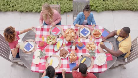 happy diverse group of friends eating and talking at dinner table in garden, slow motion