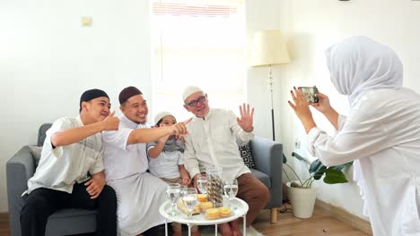 muslim woman take pictures of family members using smartphone during eid mubarak moment in the living room