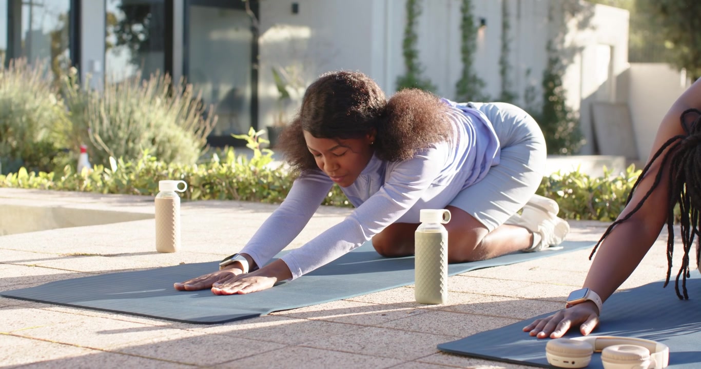 African American friends in activewear practicing forward stretch on patio with mats during warmup