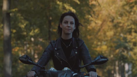 Beautiful-smiling-white-dutch-woman-on-motor-bike-driving-on-road-with-autumn-gold-leaves-colorful-Trees-in-forest-on-sunny-day