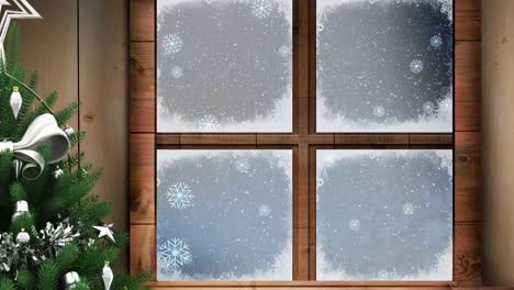 Christmas-tree-and-wooden-window-frame-against-snow-falling-over-winter-landscape