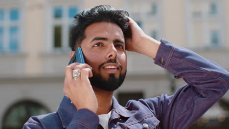 happy young man having remote conversation talking on smartphone good news gossip in city street