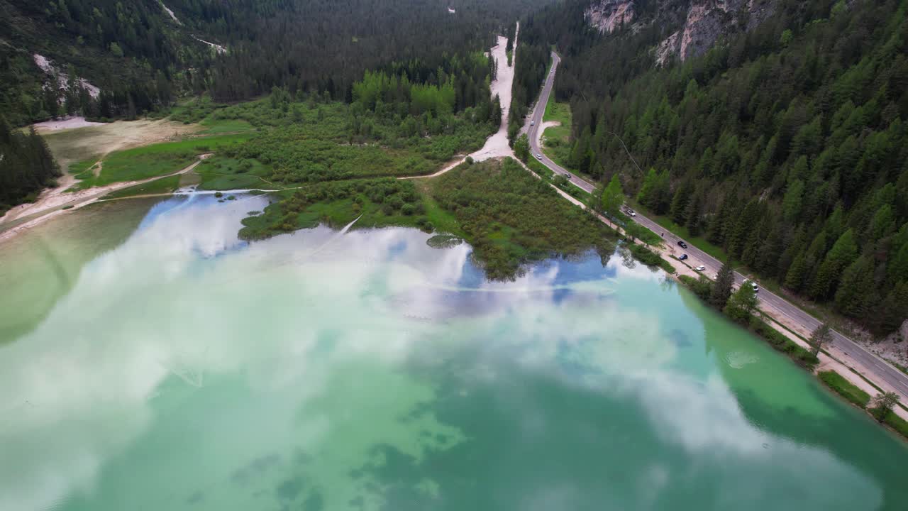 Movimento tilt-up dal cristallino Lago di Landro rivela una cima montuosa innevata, ripresa aerea.