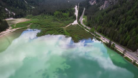 tilt-up from crystal clear lago di landro reveals snowy mountain peak, aerial