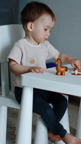 pretty little boy plays with toys sitting at desk. lovely one year old child studying animals. vertical video