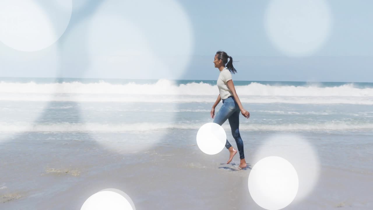 女子抬脚，海浪轻触脚趾，在沙滩上旋转，作为健康广告，伴随画面中浮动的光晕。