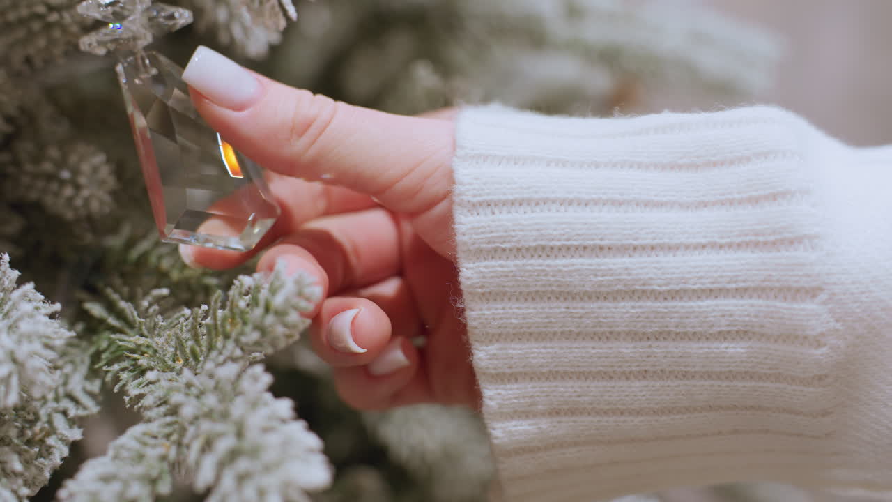 Close-up of hand in white sweater touching transparent glass decoration on Christmas tree as hand slowly removes from ornament, showing delicate details of holiday decor