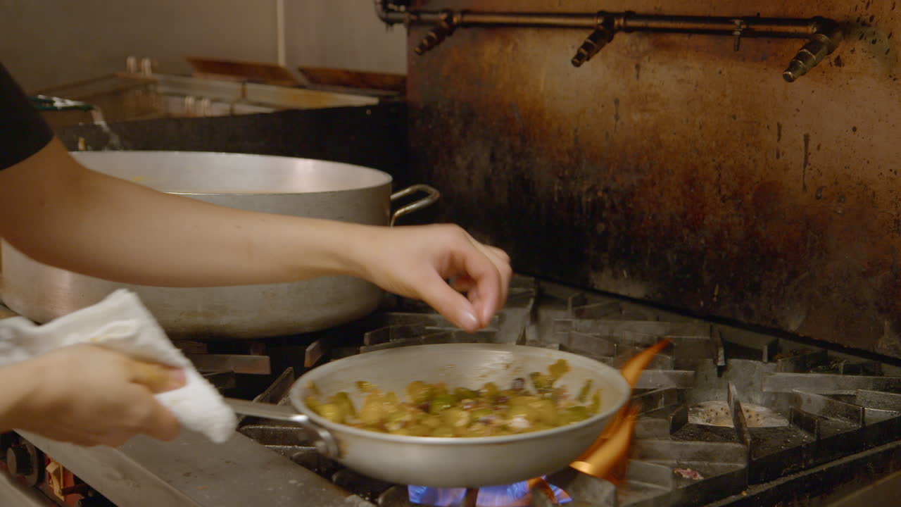 Chef tossing and mixing a stir fry over gas cooker in skillet pan
