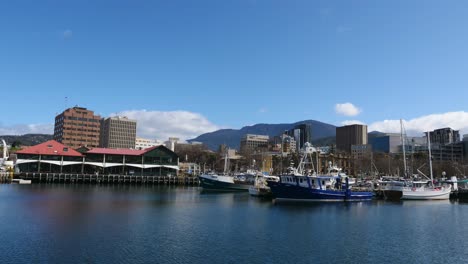 timelapse during clear sunny day at small old dock with boats and yachts tied up and building and mountains in foreground as clouds pass by