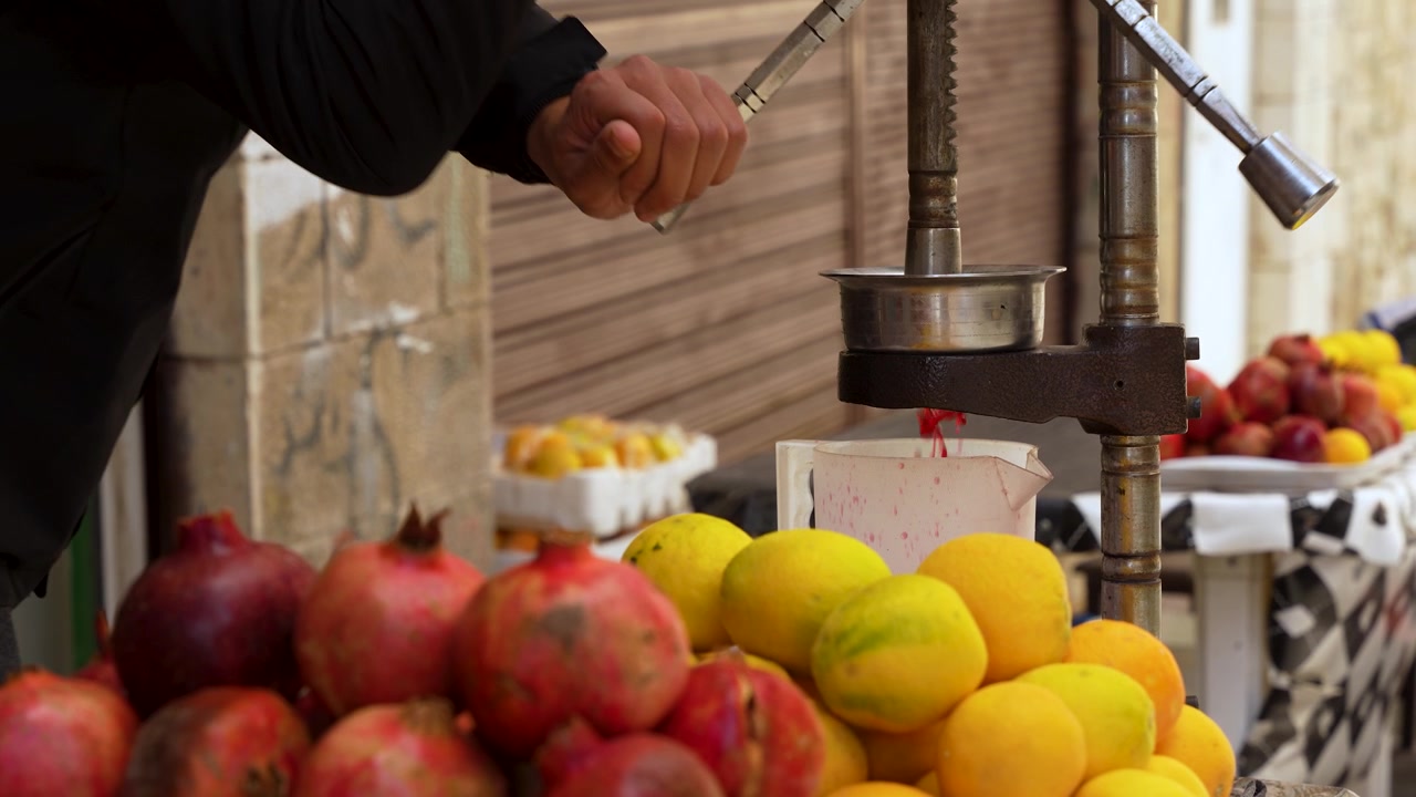 Primo piano ravvicinato, succo di melograno fresco viene preparato con uno spremiagrumi manuale in metallo in un mercato locale in Giordania, circondato da melograni maturi e agrumi.