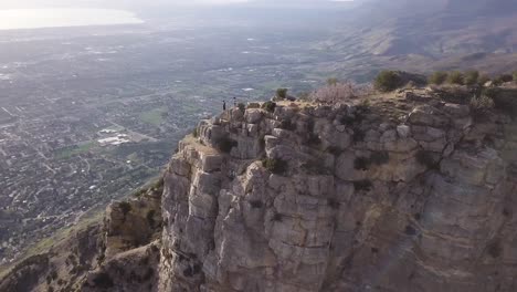 aerial orbit shot of two hikers standing on a mountain peak in provo, utah with drone panning to reveal the town below