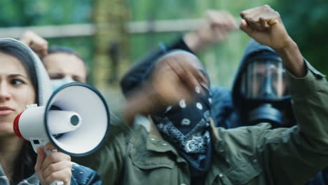 close-up view of caucasian woman in hoodie yelling on a loudspeaker in a protest with multiethnic group of people in the street