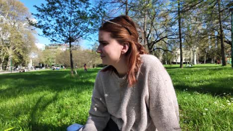 A-girl-sits-on-the-grass-in-the-park-on-a-sunny-day,-embodying-the-concept-of-relaxation-and-enjoying-nature