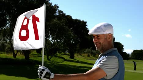 Golfista-Sonriente-Sosteniendo-La-Bandera-Del-Hoyo-18-En-El-Campo-De-Golf