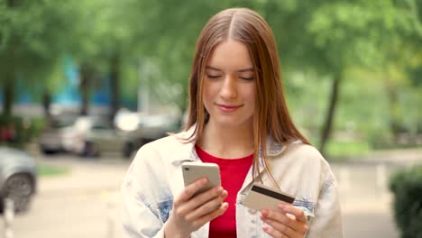 hübsche junge frau, die mit ihrem smartphone online einkauft und draußen mit kreditkarte bezahlt