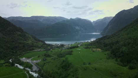 drone flies through a valley to a small norwegian village on a lake