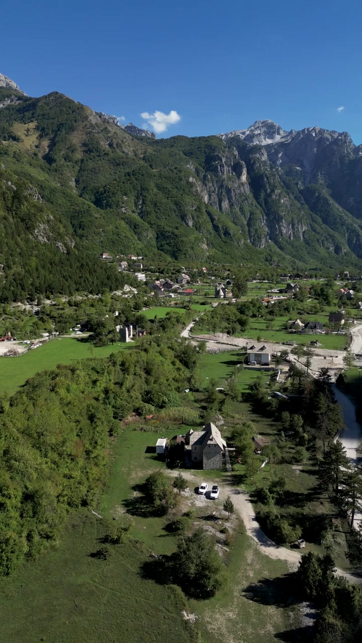Ripresa verticale con drone del villaggio di Theth nell'Albania settentrionale, che domina la storica chiesa immersa in un rigoglioso campo verde. Mette in mostra la bellezza delle Alpi Albanesi, il patrimonio rurale e il suggestivo paesaggio montano.