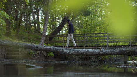 black man standing and crossing a creek on tree trunk bridge in the woods - right to left