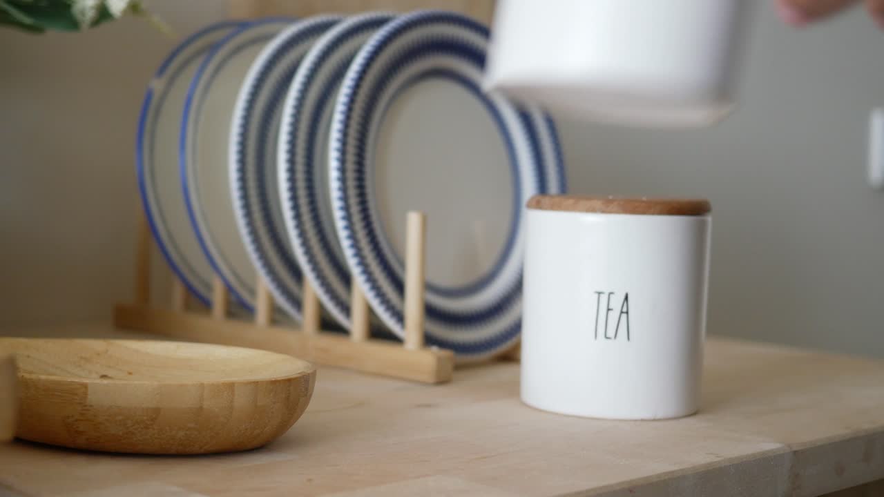 persona que alcanza los botes de azúcar y té en un mostrador de la cocina