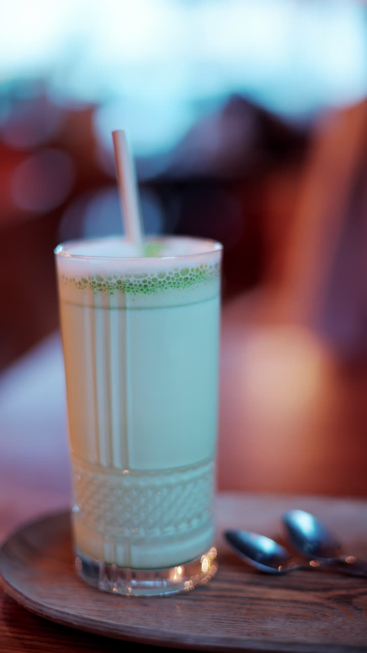 Close up of a matcha latte in a glass with a straw on a table at a cafe. Vertical