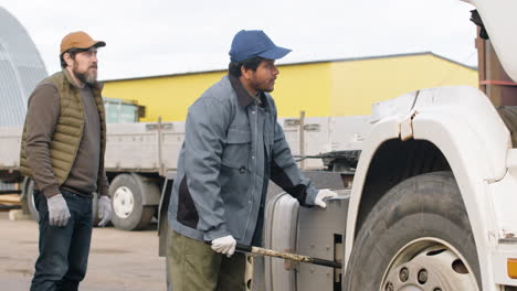 worker fixing a truck in a logistics park while being supervised by his boss