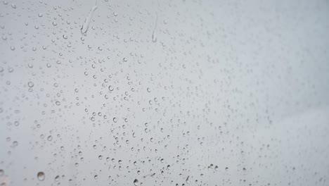 a slow-motion close-up shot of heavy rain drops is seen through a window glass